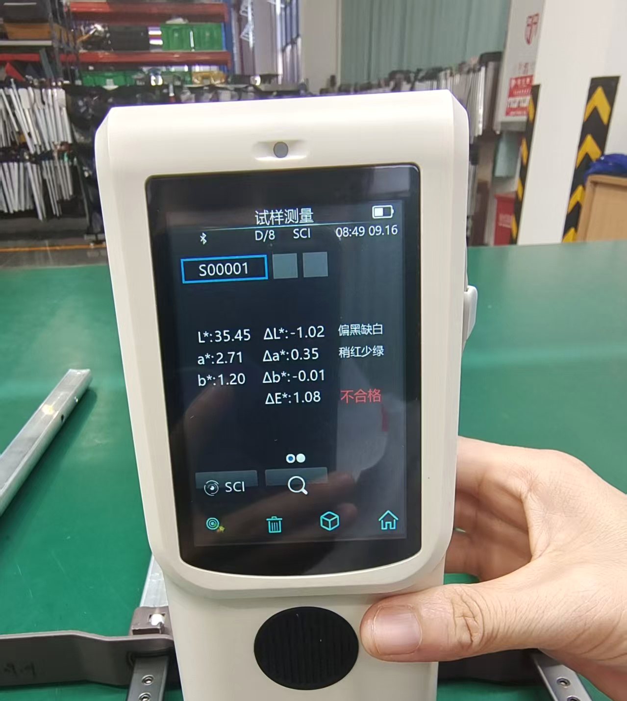 A handheld spectrophotometer held against a metal fitting, its screen showing a reading of Delta E 1.08 against standard S00001 with a failing verdict