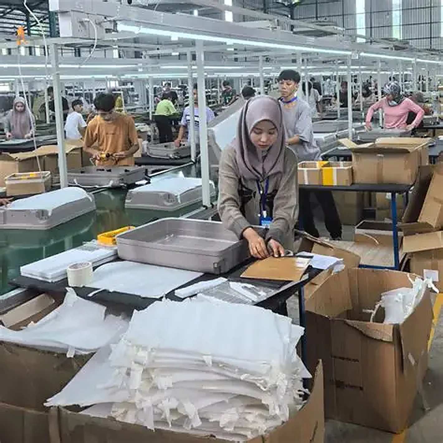 Workers assembling hardside luggage shells at stations on a first production run, with packing materials at the bench